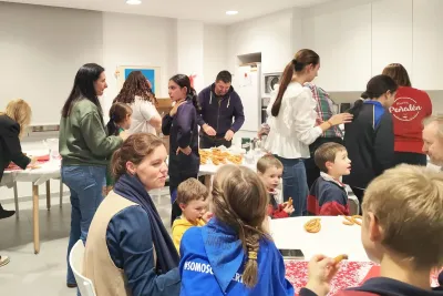 Adultos y niños reunidos, algunos comiendo dulces en una mesa.