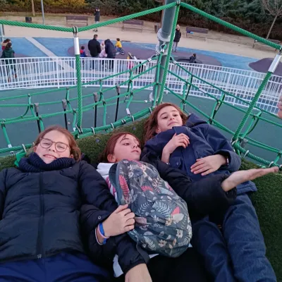 Tres niñas tumbadas y sonriendo sobre una superficie de césped artificial en una estructura de juegos.