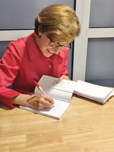 María Isabel Alvira firmando y dedicando un ejemplar de su libro con un bolígrafo sobre una mesa de madera