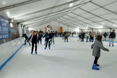 Vista general de la pista de hielo cubierta con muchas personas patinando, incluyendo niñas del club y figuras decorativas de Navidad en el fondo.