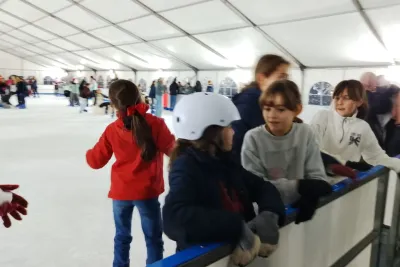 Primer plano de cuatro niñas apoyadas en el borde de la pista de hielo, una de ellas con un casco blanco.