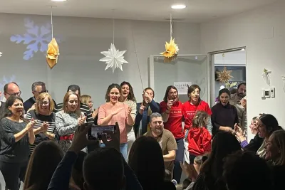 Grupo grande de adultos aplaudiendo y cantando en un evento navideño.