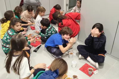 Niños comiendo churros con chocolate sentados en el suelo.