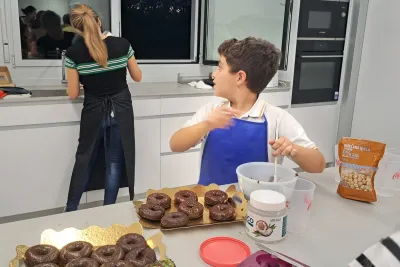 Niño decorando los donuts mientras pregunta a la cocinera, que está de espaldas.
