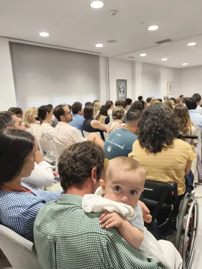 Un bebé en brazos mirando a la cámara durante una conferencia en una sala llena de público