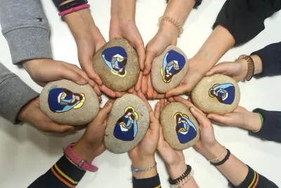 Manos en círculo sujetando piedras con una Virgen pintada