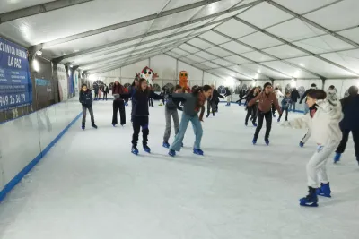 Un grupo de niñas sonrientes patinando sobre hielo dentro de una pista cubierta.