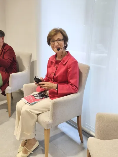 María Isabel Alvira sentada en una silla con un micrófono de diadema y su libro en el regazo