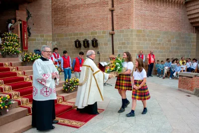 Dos niñas entregando un ramo de flores como ofrenda