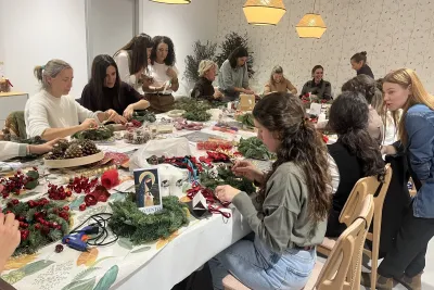 Vista general de un taller de manualidades donde varias mujeres están concentradas creando coronas de Adviento, con herramientas y materiales naturales sobre la mesa.