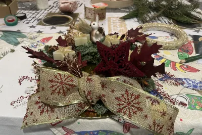 Primer plano de una corona de Adviento festiva con lazo de arpillera y copos de nieve, tres velas doradas y un adorno de ardilla blanca.