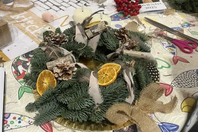 Corona de Adviento rústica de abeto con rodajas de naranja secas, plumas, adornos de madera y un lazo de arpillera natural.