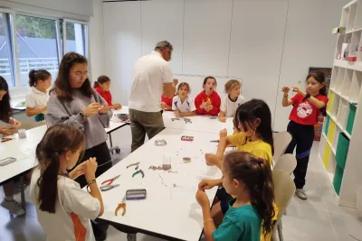 Grupo de chicas de pie alrededor de las mesas trabajando en los pendientes.