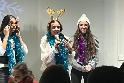 Tres jóvenes con disfraces festivos y boas cantando con un micrófono.