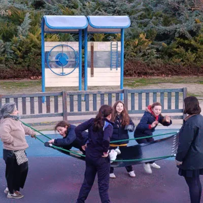 Un grupo de personas jugando y balanceándose en una hamaca grande de goma en un parque público.